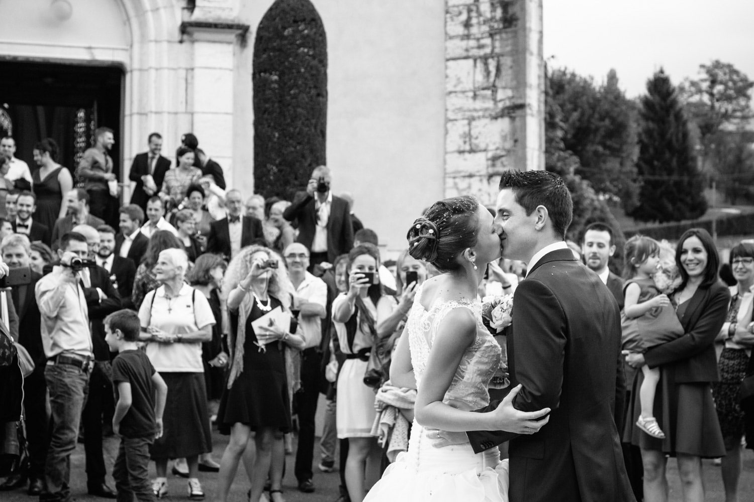 bisou des mariés de dos à la sortie de l'église